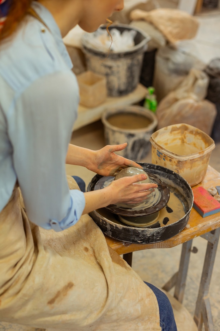 Foto equipo profesional. mujer flaca se concentra en la rueda de alfarería mientras se lo pasa en grande en el taller equipado