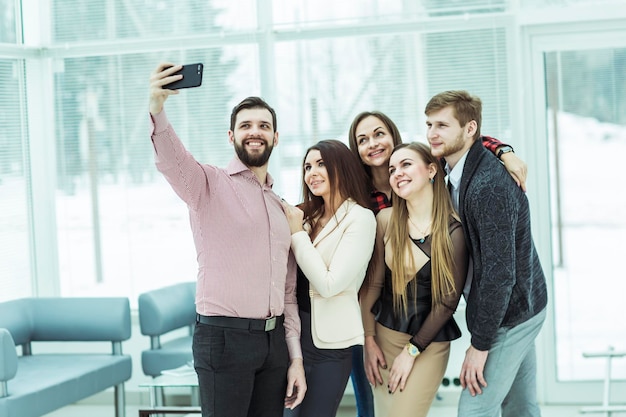 Equipo profesional de negocios haciendo selfie mientras está parado cerca de la ventana en la oficina