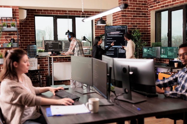 Equipo de programadores que analizan el código de la aplicación de aprendizaje automático en la pantalla grande de programación, de pie en la oficina de la empresa. Desarrolladores de software que trabajan en un sistema de base de datos con script html