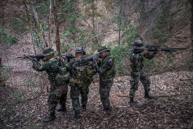 Equipo de soldado del ejército con ametralladora moviéndose en el bosqueSoldado de la milicia tailandesa con uniformes de combate en el bosquePasear por la patrulla en pendiente en la selva tropical