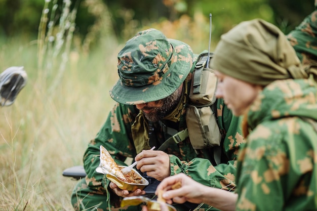 El equipo de soldados calienta la comida en el fuego y come en el bosque