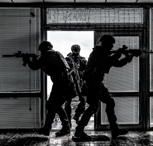 Equipo táctico de las fuerzas especiales antinarcóticos o antiterroristas de la policía que atraviesa la puerta y entra en el edificio durante la orden de búsqueda y arresto o la operación de rescate de rehenes, desaturado, alto contraste