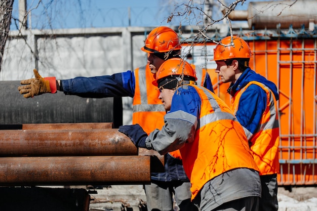 Equipo de trabajadores de la construcción en cascos discute el lugar de colocación de tuberías Tres trabajadores consultan en la calle