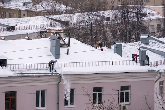 El equipo de trabajadores masculinos limpia el techo del edificio de la nieve con palas para asegurar los cinturones de mantra.