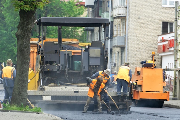 Un equipo de trabajadores con palas está trabajando en la colocación de asfalto nuevo Reparación de carreteras Trabajadores con herramientas junto a un apilador de asfalto de rodillos en la carretera durante el trabajo