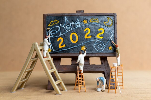 Equipo de trabajadores de personas en miniatura pintando el número 2022 en la pizarra, concepto de feliz año nuevo