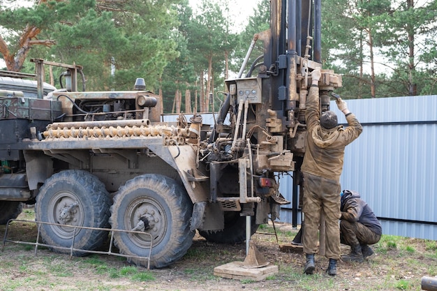 Un equipo de trabajadores con una plataforma de perforación en un automóvil está perforando un pozo artesiano para obtener agua en el suelo Inserción de una tubería de revestimiento de metal en el suelo Instalación de un suministro individual de agua potable 28 de junio de 2022 Rusia