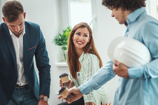 Un equipo de tres jóvenes arquitectos está tomando un café en la oficina mientras trabajan en un nuevo proyecto.