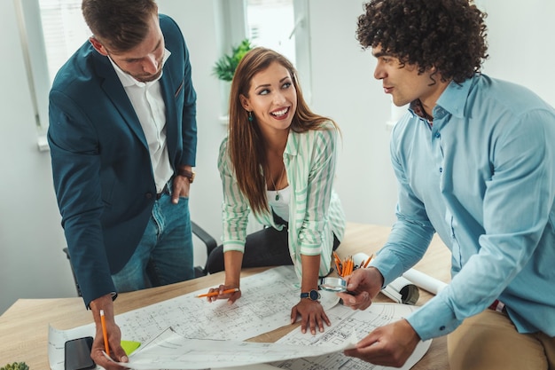 El equipo de tres jóvenes arquitectos está trabajando en un nuevo proyecto y se comunica mientras analiza planos en la oficina.