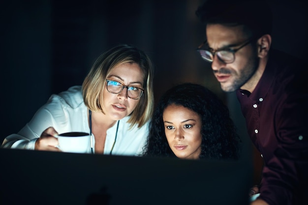 El equipo del turno de noche sabe cómo hacer las cosas Foto de un grupo de colegas usando una computadora juntos durante una noche en el trabajo