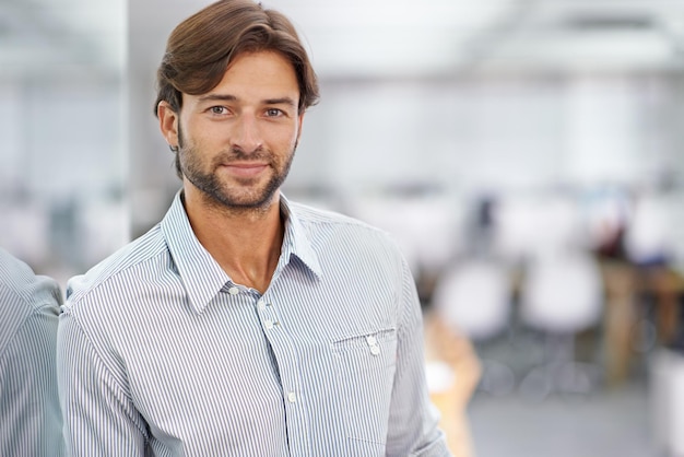 Er ist ein selbstbewusster junger Geschäftsmann. Porträt eines hübschen jungen Geschäftsmannes, der in seinem Büro steht.