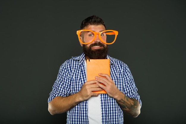 Er ist so ein Geek Student der Universität mit Vorlesungsnotizen Bärtiger Mann in Partybrille mit Lehrbuch Buchnerd mit ausgefallener Brille Studieren Sie den Nerd, der ein Buch hält