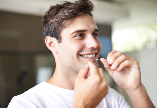 Er kennt die Bedeutung der Zahnhygiene. Nahaufnahme eines jungen Mannes, der Zahnseide verwendet