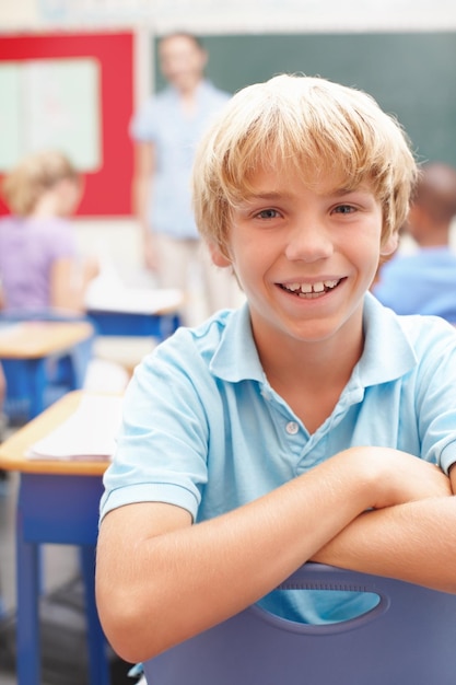 Foto er liebt den unterricht porträt eines süßen blonden schuljungen, der im unterricht an einem schreibtisch sitzt