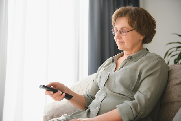 La era de la televisión tecnológica y el concepto de la gente feliz anciana viendo la televisión y cambiando de canal con control remoto en casa