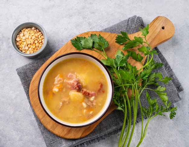 Erbsensuppe mit geräuchertem Schinken auf Schneidebrett auf hellem Hintergrund mit Kräutern