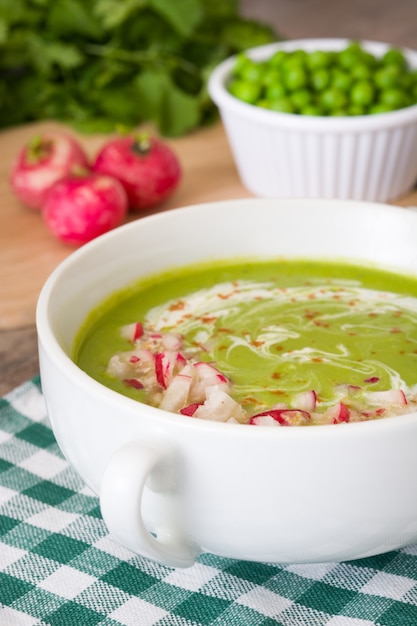 Erbsensuppe mit Radieschen auf rustikalem Holztisch