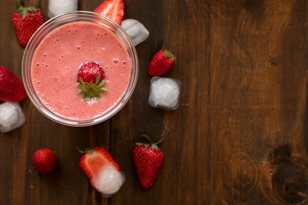 Erdbeer-Bananen-Smoothies in Gläsern mit Eiswürfeln und Zutaten auf dunklem Holztisch