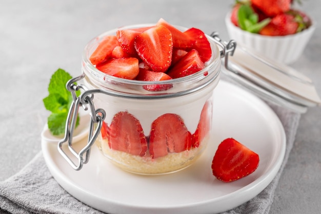 Erdbeer kein gebackener Käsekuchen im Glasgefäß mit frischen Erdbeeren oben auf einem konkreten Hintergrund