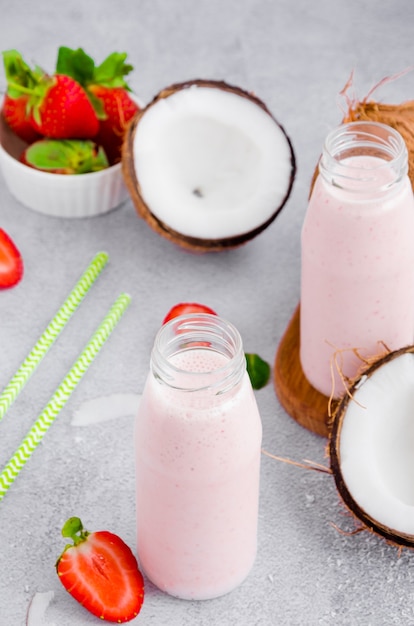 Erdbeer-Kokos-Smoothie auf Kokosmilch in einem Glas mit einem Strohhalm auf einer grauen Wand. Gesundes Lebensmittelkonzept. Vertikale Ausrichtung.