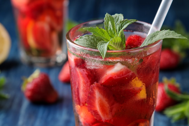 Erdbeer-Mojito. Kalter Sommer-Mojito-Cocktail mit Erdbeeren, Minze, Zitrone und Eis in einem Glas auf einem blauen Holztisch. auf dunklem Hintergrund. Nahansicht