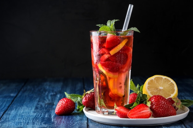 Erdbeer-Mojito. Kalter Sommer-Mojito-Cocktail mit Erdbeeren, Minze, Zitrone und Eis in einem Glas auf einem blauen Holztisch. auf dunklem Hintergrund