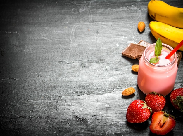 Erdbeer-Smoothie mit Beeren, Schokolade, Nüssen und Bananen. Auf dem schwarzen Holztisch.
