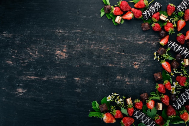 Erdbeere mit Schokolade und Süßigkeiten auf einem schwarzen Hintergrund aus Holz Draufsicht Kopieren Sie Platz