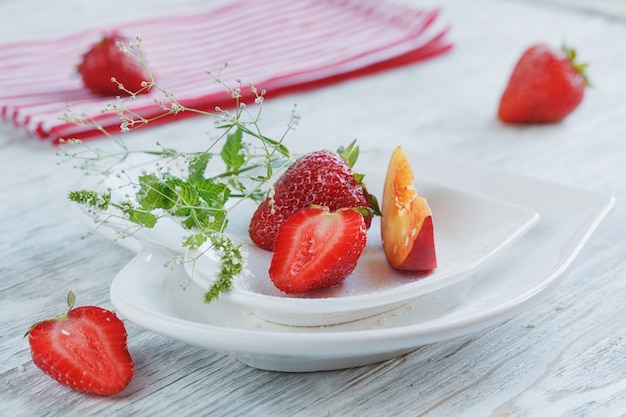 Erdbeere und Pfirsich mit Minze auf einer weißen gehörten Formplatte