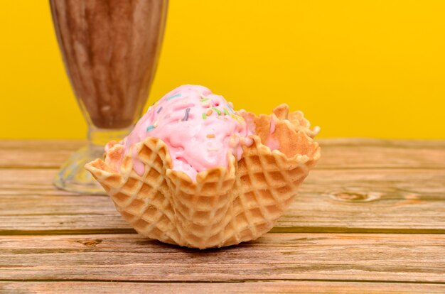 Erdbeereis im essbaren Korb Korb mit Eis auf Holztisch mit gelbem Hintergrund