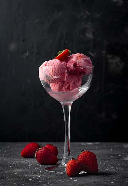 Erdbeereisbällchen mit Erdbeerbeeren, in einem hochtransparenten Glas auf einem dunklen Hintergrund
