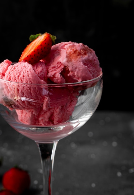 Erdbeereisbällchen mit Erdbeerbeeren, in einem hochtransparenten Glas auf einem dunklen Hintergrund