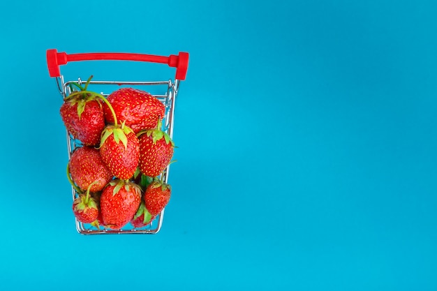 Erdbeeren in einem Einkaufswagen auf blauem Hintergrund