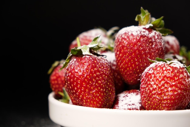 Erdbeeren in einem Teller mit Puderzucker auf schwarzem Hintergrund