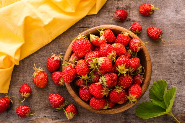 Erdbeeren in einer Holzschale und herum, Serviette und Blätter auf einem Holztisch. Ansicht von oben