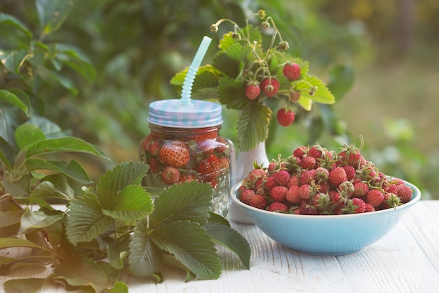 Erdbeeren in Schüssel und Cocktail in einem Glas auf einem Holztisch im Garten bei Sonnenuntergang