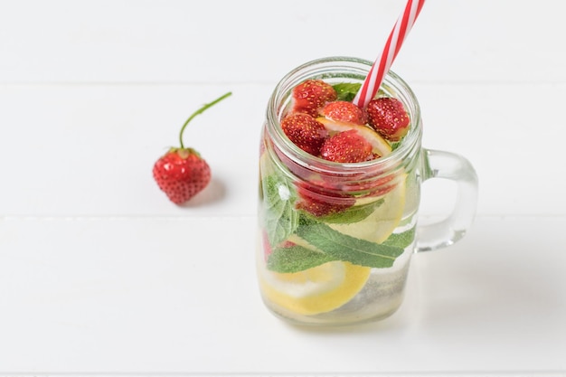 Erdbeeren und eine Tasse kaltes Wasser mit Beeren und Zitrone