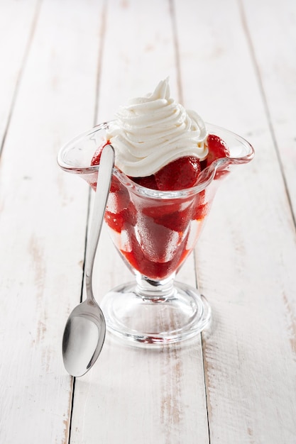 Erdbeeren und Schlagsahne im Eisglas auf Holztisch