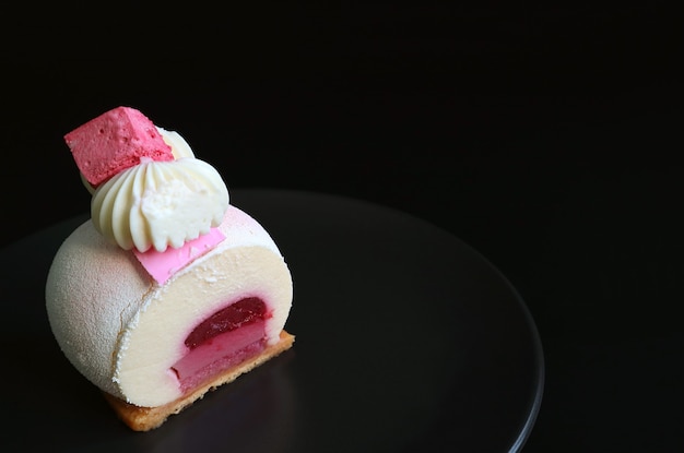 Erdbeergelee-Vanille-Mousse-Kuchen auf schwarzem Teller mit Kopierraum auf schwarzem Hintergrund