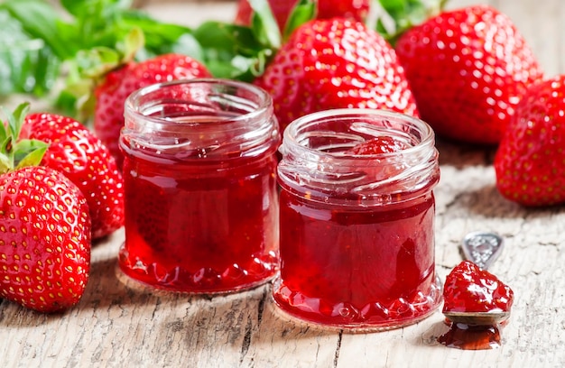 Erdbeerkonfitüre mit ganzen Beeren und frischen Erdbeeren auf einem alten hölzernen Hintergrund im selektiven Fokus der rustikalen Art