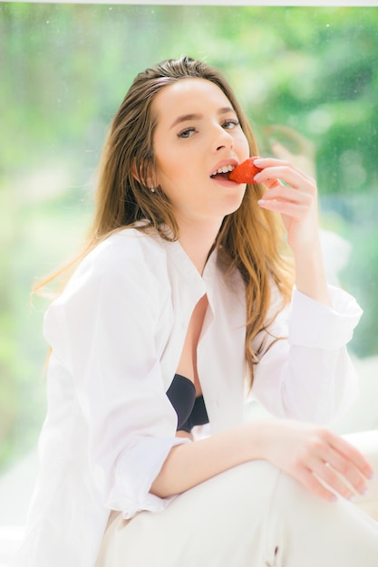 Erdbeerlippen Schöne junge hemdlose Frau, die Erdbeere in ihrer Hand hält und schmeckt