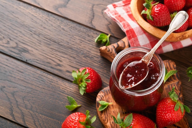 Erdbeermarmelade Erdbeermarmelade im Glas mit frischen Beeren auf einem alten Holztisch mit dunklem Hintergrund Nahaufnahme Hausgemachte fruchtige Erdbeermarmelade Draufsicht mit Kopierbereich