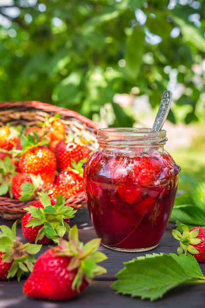 Erdbeermarmelade und saftige reife Erdbeeren auf einem Holztisch im Garten auf einer Sommersonne