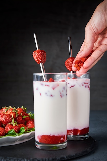 Erdbeermilch-Smoothie im Glas mit Stroh und frischen Beeren auf Schwarz