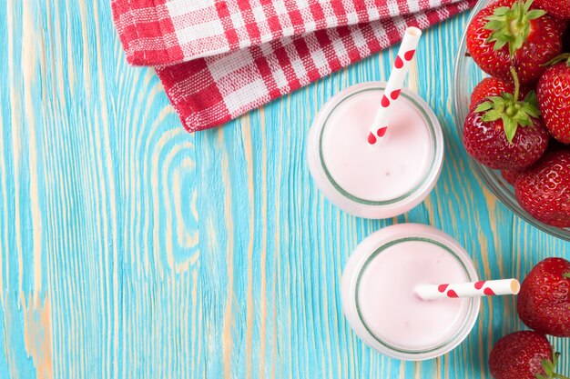 Erdbeermilchshake im Glas mit Trinkhalm auf blauem Holztisch. Draufsicht