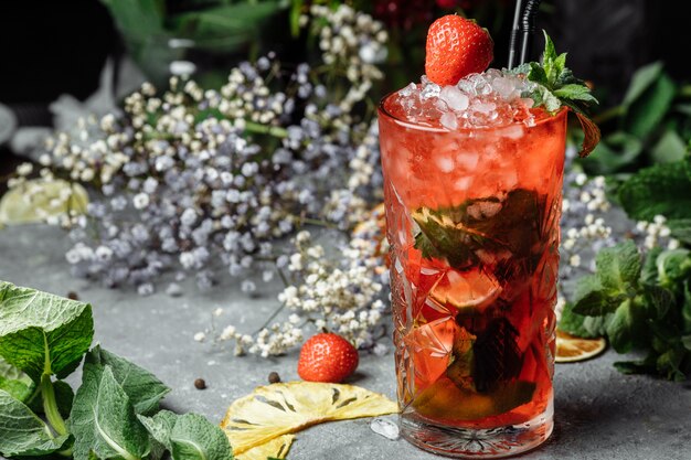 Erdbeermojito. Kalter Sommer-Mojito-Cocktail mit Erdbeeren, Minze, Zitrone und Eis in einem Glas auf einem Tisch.