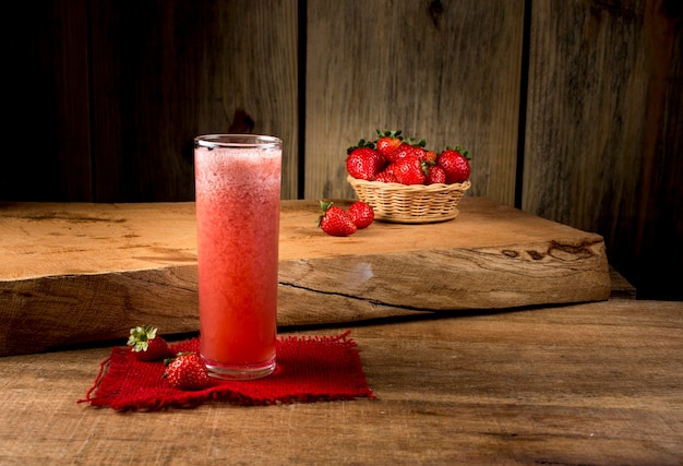 Erdbeersaft im Glas auf Holz mit Erdbeerkorb im Hintergrund.