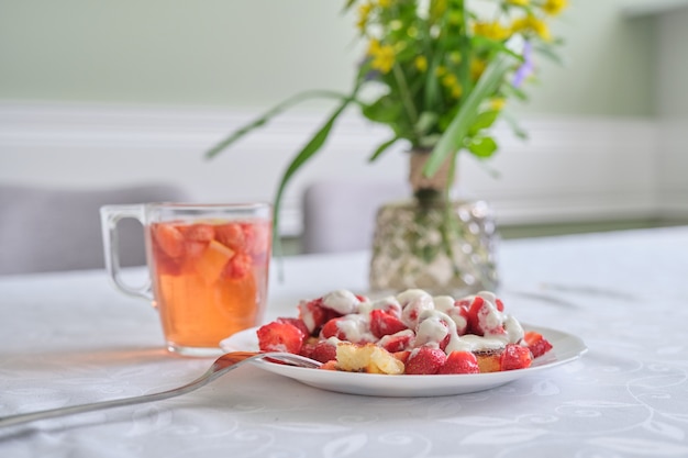 Erdbeersaison, Essen und Trinken mit Beeren. Essen auf dem Tisch, Quarkpfannkuchen mit Erdbeeren und Sauerrahm. Tee mit Zitrone und Beeren