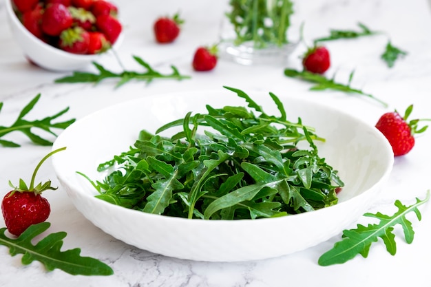 Foto erdbeersalat mit rucola-spinatblättern auf marmortisch mit salat und erdbeerfrüchten