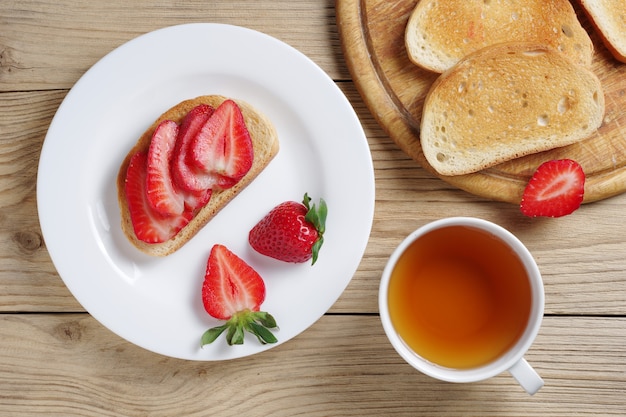 Erdbeersandwich und Tasse Tee auf Holztisch, Draufsicht